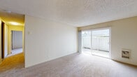 This 2-bedroom, 1-bathroom unit is thoughtfully arranged on a single floor, offering a functional and comfortable layout throughout. The living room is a bright, open space featuring wall-to-wall carpet, a textured ceiling, and a full-width sliding glass door that opens to a private, fenced outdoor area, allowing natural light to fill the room. The galley-style kitchen is efficiently designed with rich wood cabinetry lining both sides, dark granite-style countertops, hardwood-style flooring, and a full suite of black appliances including a range, dishwasher, and refrigerator, all beneath warm overhead lighting. Both bedrooms are carpeted and generously sized, each benefiting from natural light through well-placed windows. One bedroom features a built-in closet system with shelving and hanging rods, providing ample storage. The shared bathroom includes a combination tub and shower enclosed by sliding frosted glass doors with tile surround, complemented by a wood-toned vanity and hardwood-style flooring. Throughout the unit, neutral tones and textured ceilings create a clean, cohesive aesthetic suited for comfortable everyday living.