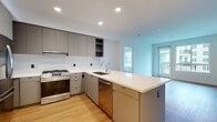 Located at 201 Del Sol Dr in San Diego's Mission Valley area, this single-floor residence showcases a clean, modern design throughout. The open-concept kitchen is a standout feature, equipped with full-height grey flat-front cabinetry, stainless steel appliances including a gas range, refrigerator, and dishwasher, complemented by a crisp white quartz countertop and a peninsula that extends into the living area. A tasteful tile backsplash and recessed lighting complete the kitchen's contemporary aesthetic. Warm wood-look flooring runs throughout the space, tying each room together cohesively. The bedrooms are bright and airy, each featuring large windows that invite natural light and offer views of the surrounding urban community. Spacious closet areas with full-width hanging rods provide ample storage. Two bathrooms are finished in a minimalist style, each with white quartz vanity surfaces, undermount sinks, modern fixtures, and large backlit mirrors. One bathroom includes a tiled tub-shower combination. A dedicated in-unit laundry area with a stacked washer and dryer adds everyday convenience. Recessed lighting and neutral white walls throughout give the space a fresh, move-in-ready feel.
