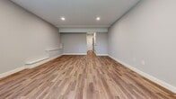 This three-floor home offers a thoughtfully designed layout across three spacious levels. The ground floor provides a welcoming entrance that opens into a bright living area featuring hardwood flooring, recessed lighting, a ceiling fan, a corner fireplace with tile surround, and sliding glass doors leading to an outdoor space with wooded views. The kitchen is a standout, equipped with slate-gray shaker cabinetry, a white subway tile backsplash, stainless steel appliances, a kitchen island with pendant lighting, and warm hardwood floors that flow seamlessly into the adjacent dining and living areas. The bathrooms are finished with gray shaker vanities, matte black hardware, light tile flooring, and clean white fixtures. The bedrooms are carpeted and well-lit, featuring ceiling fans and windows that frame natural outdoor views. The primary bedroom offers a comfortable, generously sized retreat. Upper-level spaces include additional bedrooms and a more intimate living area. A utility room, closet, and multiple hallways add practical functionality throughout. The home's consistent use of soft gray walls, hardwood and carpet flooring, recessed lighting, and matte black accents creates a cohesive, modern aesthetic throughout all three floors.