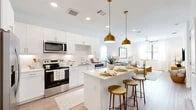 This single-story unit offers a thoughtfully planned layout across a comfortable footprint, accommodating one bedroom and three full bathrooms. The open-concept kitchen and living area serves as the heart of the unit, where light wood-tone flooring, recessed lighting, and natural light from multiple windows create a bright, welcoming atmosphere. The kitchen is outfitted with white shaker cabinetry extending to the ceiling, a white subway tile backsplash, stainless steel appliances including a refrigerator, range, microwave, and dishwasher, and a center island with a light quartz countertop. Gold pendant lights above the island add a warm, modern accent. The living area flows seamlessly from the kitchen and features a ceiling fan and natural light from large windows.

The bedroom is carpeted and well-lit by natural light, with windows providing an open feel. Two closets serve the unit, including a walk-in closet with built-in shelving and hanging rods, accessible through one of the bathrooms. The bathrooms are finished in a clean, white palette with wood-look flooring, white vanities with quartz countertops, and tub-shower combinations with white tile surrounds. The overall aesthetic throughout is modern and cohesive, emphasizing clean lines and a neutral color palette.