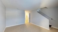 Located at 2415 West, this two-story property offers a straightforward and functional layout spread across two floors. The main living area is characterized by light gray walls, neutral-toned tile flooring, and a clean, minimalist aesthetic that creates a bright and airy atmosphere. A staircase is prominently positioned along one wall, providing easy access to the upper level. The open sightlines from the main room extend through a doorway into an adjacent space, suggesting a connected and practical floor plan. Overhead, the smooth white ceiling with a ceiling vent contributes to the well-maintained, move-in-ready feel of the space. The interior benefits from a neutral color palette throughout, lending itself well to a variety of furnishing styles. The transition between rooms is seamless, with white-painted doors and trim adding a crisp finishing detail. Overall, the property presents a simple, clean environment with consistent finishes across its two floors, making it a versatile space suitable for a range of uses.