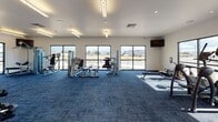 Located at 2665 Kingsgate Way in Richland, Washington, this single-floor fitness center is designed to accommodate a wide range of workout needs in a clean, modern environment. The facility is divided into two distinct areas: a main gym floor and a dedicated group fitness or stretching studio.

The main gym floor is carpeted in deep blue and bathed in natural light through large windows that line the perimeter walls, offering views of the surrounding area. The space is well-equipped with a full row of treadmills and elliptical machines along the cardio section, complemented by a comprehensive strength training zone featuring a power rack, cable machines, weight benches, and a tiered dumbbell rack. Wall-mounted televisions are positioned throughout for user convenience. A small utility area with cabinetry and a sink provides added functionality.

The adjacent group fitness studio features smooth hardwood-style flooring and is enclosed with full-length wall mirrors that enhance the sense of openness. This room includes a storage rack stocked with stability balls in various sizes, making it well-suited for yoga, group classes, stretching, or individual floor-based workouts.

Throughout the facility, white walls and bright overhead lighting create a clean, energizing atmosphere. The thoughtful layout efficiently separates cardio, strength, and flexibility training zones.
