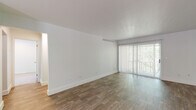 This single-floor residence offers a clean, functional layout with a neutral palette throughout. The spacious living area is finished with wood-style flooring and features a large sliding glass door fitted with vertical blinds, allowing generous natural light and views of surrounding greenery. A front entry door opens directly into this open living space, which flows seamlessly into the rest of the home.

The kitchen is equipped with warm-toned wooden cabinetry, light speckled countertops, a coil-element range with oven, a dishwasher, and a utility sink — providing a practical and well-organized cooking environment. An adjacent secondary room, also with wood-style flooring and a window overlooking the outdoors, offers flexible use as a dining area or additional living space.

The bedrooms are carpeted for comfort and feature windows that bring in natural light. The primary bedroom is notably well-appointed with an extensive wall of louvered bi-fold closet doors, offering generous storage capacity.

The bathroom presents a clean, all-white aesthetic with a full tub and shower combination, white tile surround, and a window for ventilation and natural light. Throughout the space, crisp white walls, consistent trim work, and practical finishes contribute to a bright, move-in ready environment.