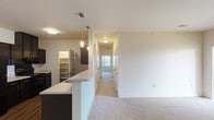 This single-floor residence offers a clean, modern layout designed for comfortable everyday living. The kitchen serves as a central hub, featuring dark espresso cabinetry, black appliances including a refrigerator and range, durable hardwood-style flooring, and a generous walk-in pantry with built-in shelving. A white peninsula counter extends into the living area, providing additional prep space and a natural transition to the open living and dining zones. The entryway is defined by a hardwood-style tile threshold that contrasts with the soft, neutral carpeting found throughout the rest of the home.

The living area is bright and open, with access to a private balcony through a glass-panel door, allowing for natural light and outdoor views of the surrounding community. Multiple bedrooms offer comfortable proportions, each featuring plush carpet, neutral walls, and windows fitted with horizontal blinds. One bedroom benefits from dual windows that invite ample natural light.

Two bathrooms serve the residence, each finished with dark vanity cabinetry, light countertops, single-basin sinks, and hardwood-style flooring. One bathroom includes a large mirror and access to additional closet storage. A hallway connects the living spaces to the bedrooms, keeping the floor plan organized and functional throughout.