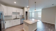 This well-designed 2-bedroom, 2-bathroom residence offers a thoughtful single-floor layout that balances functionality with modern style. The open-concept kitchen serves as the heart of the home, featuring crisp white shaker cabinetry, a subway tile backsplash, a large center island with quartz countertops, and a full suite of stainless steel appliances including a refrigerator, range, microwave, and dishwasher. Elegant pendant lighting hangs above the island, while recessed lighting illuminates the space throughout. A dedicated pantry provides additional storage. The kitchen flows seamlessly into the living area, which is bathed in natural light from wide windows and finished with wood-style flooring and a ceiling fan. A hallway connects the bedrooms, with wood-style flooring continuing throughout. The primary bedroom is generously sized, featuring a ceiling fan, natural light from side windows, a walk-in closet, and a private en-suite bathroom with a double vanity, framed mirror, and a glass-enclosed shower. The second bathroom includes a tub-shower combination and a vanity with quartz countertops. Neutral tones, clean lines, and consistent finishes give the entire residence a cohesive, contemporary feel.