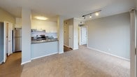 Located at 4795 Frazee in Oceanside, unit #1414 is a single-floor residence designed with a practical, open-concept layout that maximizes the available living space. The unit is finished in a neutral gray and white color palette throughout, creating a clean, cohesive aesthetic.

The kitchen is a standout feature, offering generous counter space with dark granite-style countertops, white shaker-style cabinetry, and a full suite of stainless steel appliances including an electric range with overhead ventilation, a refrigerator, dishwasher, and built-in microwave. The kitchen opens directly to the main living area via a half-wall peninsula, enhancing the sense of flow between spaces. Wood-look flooring runs through the kitchen, while plush carpeting covers the living area.

The living room is spacious and bright, featuring crown molding, a ceiling fan, track lighting, and a large sliding glass door with vertical blinds that opens to a private balcony with outdoor views of surrounding greenery. A secondary window adds additional natural light.

The bathroom is clean and functional, featuring a combined tub and shower with tiled surround and chrome fixtures. The unit also includes an in-unit laundry area with space for a full-size washer and dryer. Overall, the space offers a comfortable, well-appointed living environment.