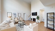 Located at The Villas at Setauket in East Setauket, NY, this two-story villa offers a thoughtfully designed layout with high-end finishes across both floors. The main living area immediately impresses with soaring double-height ceilings, warm hardwood flooring, and a gas fireplace as a central focal point. A staircase with a wood handrail connects the two levels, adding architectural character to the open layout.

The dining area is bathed in natural light from multiple windows framed with white blinds, and is anchored by a striking industrial-style orb chandelier above a substantial wood dining table. The kitchen features white shaker cabinetry extending to the ceiling, crisp quartz countertops, and stainless steel appliances including a gas range, over-the-range microwave, and a French door refrigerator.

The bedrooms are generously proportioned, with the primary suite offering hardwood flooring and ample natural light, while a secondary bedroom features plush carpeting and bright window access. The bathroom is finished with marble-patterned tile flooring, a white vanity with a dark countertop, and a tub-shower combination with elegant marble-style surround tile. An attached garage with an automatic opener completes this well-appointed home.