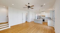 Located at 115 Gaunt Ln in Youngsville, Louisiana, this two-story home offers a thoughtfully designed layout spread across two floors. The main level houses the open-concept kitchen and living area, where warm hardwood-style flooring flows throughout. The kitchen stands out with crisp white shaker cabinetry, a large center island with quartz countertops, stainless steel appliances including a French door refrigerator and gas range, and elegant gold pendant lighting overhead. Recessed lighting and multiple windows bring in ample natural light, while a door provides direct access to the covered outdoor area. The exterior features a covered patio, fenced surroundings, and a concrete driveway with an attached garage. A wood-tread staircase with clean white risers connects both levels seamlessly. Upstairs, two well-proportioned bedrooms feature ceiling fans, recessed lighting, and the same warm hardwood-style flooring. The spacious primary bedroom is complemented by a dedicated closet with double hanging rods. The four bathrooms include finishes such as penny-tile flooring and a soaking tub with shower combination featuring matte black fixtures. A laundry area and ample closet storage add to the home's everyday functionality.