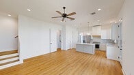 Located at 115 Gaunt Ln in Youngsville, Louisiana, this two-story home offers a thoughtfully designed layout spread across two floors. The main level houses the open-concept kitchen and living area, where warm hardwood-style flooring flows throughout. The kitchen stands out with crisp white shaker cabinetry, a large center island with quartz countertops, stainless steel appliances including a French door refrigerator and gas range, and elegant gold pendant lighting overhead. Recessed lighting and multiple windows bring in ample natural light, while a door provides direct access to the covered outdoor area. The exterior features a covered patio, fenced surroundings, and a concrete driveway with an attached garage. A wood-tread staircase with clean white risers connects both levels seamlessly. Upstairs, two well-proportioned bedrooms feature ceiling fans, recessed lighting, and the same warm hardwood-style flooring. The spacious primary bedroom is complemented by a dedicated closet with double hanging rods. The four bathrooms include finishes such as penny-tile flooring and a soaking tub with shower combination featuring matte black fixtures. A laundry area and ample closet storage add to the home's everyday functionality.