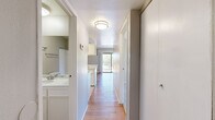 Located at 45278 Deep Canyon Rd in Palm Desert, California, this one-bedroom, one-bathroom unit offers a well-organized, efficiently designed single-floor layout. The living room serves as the heart of the space, featuring warm hardwood flooring, a textured ceiling, and a ceiling fan with light fixture. A full-width sliding glass door opens to a private patio, flooding the room with natural light and offering views of the surrounding palm trees — a fitting nod to the desert surroundings.

The kitchen is positioned adjacent to the living area, separated by a pass-through counter with a breakfast bar overhang. White cabinetry and open shelving above the counter provide functional storage, while the layout allows for easy interaction between the kitchen and living space.

A hallway connects the main living area to the bedroom and bathroom. The bedroom is carpeted for comfort, with a window fitted with vertical blinds that frame views of the palm-lined exterior. A dedicated closet with a hanging rod offers practical storage.

The bathroom features a white vanity with a stone-patterned countertop, an undermount sink, a large mirror, and a shower/tub combination. Neutral tones throughout create a clean, cohesive aesthetic well-suited to the sunny Palm Desert climate.