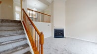 This two-story home is designed with an open and airy feel, highlighted by soaring ceilings that are most dramatic in the main living area. The living room serves as a central gathering space, anchored by a corner fireplace with a dark stone surround and a classic mantel. A carpeted staircase with warm-toned oak banisters and spindles leads to the upper level, where an open railing overlooks the main floor below, enhancing the sense of vertical space. A pendant chandelier illuminates the upper landing area.

The kitchen is functional and well-equipped, featuring white cabinetry, dark granite countertops, a center island with matching granite, hardwood flooring, and white appliances. Track lighting and a skylight-style fixture provide ample illumination throughout.

The upper level hosts multiple bedrooms, each carpeted and naturally lit by sizeable windows that offer views of the surrounding neighborhood. The bathrooms are finished in neutral tones, with tile flooring, white vanities, and generous mirror space. One bathroom includes a soaking tub alongside a separate glass-enclosed shower, while another offers a tub-shower combination. Throughout the home, a consistent neutral color palette and clean finishes create a cohesive, move-in-ready atmosphere.