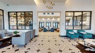 Located at 16210 Allura Cir in Naples, FL, this single-story clubhouse serves as the social and administrative hub of the Allura community. The grand entrance lobby immediately impresses with soaring ceilings, a striking geometric-patterned tile floor, and a cascading cluster pendant chandelier that sets an upscale tone. Large black-framed glass doors and windows flood the space with natural light while offering views of the surrounding outdoor areas.

The main lounge area features an open, airy layout with contemporary furnishings, including plush sofas, teal channel-back accent chairs, and warm wood coffee tables arranged atop patterned area rugs. Adjacent to the lounge is "The Alley," a stylishly branded co-working and social bar area complete with a large marble-topped island, sleek blue barstools, built-in cabinetry, a wet bar, live greenery wall accents, and glass-partitioned meeting rooms.

The dining area is equipped with generously sized tables surrounded by upholstered seating, pendant lighting, and floor-to-ceiling glass doors that open to views of the resort-style pool and lush Florida landscaping. A sophisticated leasing office features textured accent walls, bold curated artwork, and a comfortable seating arrangement. Throughout, light wood-look flooring, curated décor, and a cohesive coastal-modern palette create a welcoming and refined atmosphere.