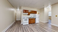 This single-floor unit at 1551 Bryden Rd in Columbus, Ohio offers a straightforward and functional layout throughout. The kitchen is equipped with warm-toned wooden cabinetry, a white electric range, a full-size refrigerator, and a sink with a granite-style countertop. A drop ceiling with recessed panels runs throughout the common areas, complementing the light-toned luxury vinyl plank flooring that flows through the kitchen and main living spaces.

The living area is open and well-proportioned, with neutral cream-colored walls and LVP flooring that extends into adjacent rooms. Multiple additional rooms feature plush carpeting, baseboard heaters for supplemental warmth, and window-mounted air conditioning units, providing individual climate control. Each room benefits from windows fitted with blinds, allowing natural light while maintaining privacy.

The bathroom is cleanly appointed with LVP flooring, a white vanity with a light countertop, a toilet, and a full tub-shower combination with a curtain rod and grab bar. The overall color palette throughout the unit is neutral and understated, with cream and beige tones on the walls. The space presents a clean, move-in-ready environment suited for practical, everyday living.