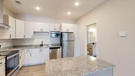 Located at 300 Hickory Trace Ln in Garner, North Carolina, this single-floor residence offers a thoughtfully designed layout with modern finishes throughout. The kitchen is a standout feature, showcasing crisp white cabinetry with matte black hardware, granite countertops, and a full suite of stainless steel appliances including a refrigerator, dishwasher, microwave, and electric range with a sleek wall-mounted hood vent. Light wood-look flooring runs through the kitchen and main living areas, creating a clean, cohesive aesthetic. The living space is carpeted and features a ceiling fan, with an entry door highlighted by a modern smart lock. Additional carpeted rooms offer generous proportions, with large windows that invite natural light and provide views of the surrounding area. The bathroom is well-finished with granite-topped white vanity cabinetry, wood-look flooring, and a full tub-shower combination with tiled surround. A secondary bathroom with matching finishes is conveniently accessible from the kitchen area. Neutral warm-toned walls, recessed lighting, and consistent trim details throughout contribute to a bright, clean, and move-in-ready atmosphere that suits a variety of lifestyles.