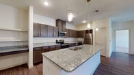 This single-floor residence offers a thoughtfully designed layout that balances functionality and modern style throughout. The centerpiece of the home is a generously sized kitchen, featuring rich dark-toned shaker cabinetry, granite countertops with subtle veining, and a large central island complete with a built-in sink and pendant lighting above. Stainless steel appliances — including a refrigerator, range, and microwave — complement the contemporary aesthetic, while a decorative wine rack adds a refined touch. Wood-look flooring runs through the kitchen and living areas, lending warmth and cohesion.

The open living room is bright and welcoming, with a ceiling fan, French doors that invite natural light, and a charming arched passage leading to a built-in shelving nook. Bedrooms are carpeted for comfort, each offering ceiling fans and windows with outdoor views. Closet space is well-considered, with one bedroom benefiting from a walk-in closet featuring built-in shelving.

The bathrooms are finished to match the kitchen's style, with dark cabinetry, granite-topped vanities, and wood-look flooring. One bathroom includes a glass-enclosed shower, while another offers a tub-shower combination. Throughout the space, neutral walls and consistent finishes create a clean, cohesive atmosphere.