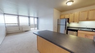 This upgraded 2-bedroom, 1-bathroom residence offers a well-designed single-floor layout that balances comfort and functionality. The open-concept living and dining area is anchored by plush carpeting and large floor-to-ceiling sliding glass doors that lead to a private balcony, flooding the space with natural light and providing expansive outdoor views.

The kitchen is a standout feature, outfitted with stainless steel appliances including a refrigerator, electric range, built-in microwave, and dishwasher. Light maple cabinetry provides ample storage, while dark countertops offer a stylish contrast. A peninsula island extends into the living area, creating a seamless connection between the kitchen and main living space.

The bathroom is clean and functional, featuring a full tub-shower combination, an oak wood vanity with under-sink storage, a wall-mounted medicine cabinet with a framed mirror, and warm accent lighting.

Both bedrooms are thoughtfully positioned within the layout, offering comfortable proportions and privacy. The neutral color palette throughout — including white walls and light carpet — creates a bright, cohesive ambiance that makes the space feel open and inviting. Overall, this upgraded residence delivers a practical yet polished living environment.
