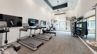 This fitness center at 401 S Fourth St in Nashville, Tennessee, offers a well-equipped exercise space designed for a comprehensive workout experience. The room features soaring ceilings accentuated by a striking recessed ceiling detail with a modern ceiling fan, contributing to an open and airy atmosphere. Crisp white walls and neutral-toned carpet flooring create a clean, contemporary aesthetic throughout.

The cardio zone is equipped with multiple treadmills and elliptical machines from Life Fitness, each paired with individual flat-screen monitors for entertainment during workouts. A wall-mounted flat-screen TV provides additional viewing options. The strength training area offers a multi-functional cable and rack system, TRX suspension trainers, a dumbbell rack, a stationary bike, an adjustable bench, and stability balls, providing a wide range of training options. Full-length mirrors along one wall enhance the sense of space and allow for form checks during exercise.

Natural light filters in through roller-shade windows, adding to the bright and inviting environment. A built-in water fountain and drinking station with subway tile surround is conveniently located near the entrance. Recessed lighting provides consistent illumination throughout the space, ensuring a well-lit setting at any time of day.