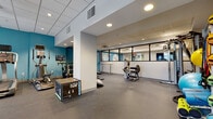 This fitness center in Hartford, CT is a thoughtfully designed, single-floor facility offering a comprehensive workout environment. The space is divided into distinct functional zones, each catering to different aspects of physical training. Durable rubber flooring spans the entire facility, providing both safety and practicality throughout all areas.

The cardio zone features a treadmill, stair climber, elliptical, and stationary bikes, each equipped with individual screens for entertainment or workout tracking. A vibrant teal accent wall anchors this section, adding energy to the space. Nearby, a dedicated strength area houses a multi-station cable machine, a adjustable weight bench, a rack of kettlebells, resistance bands, and stability balls, offering a full range of resistance training options.

A glass-partitioned studio space provides a semi-private area suitable for stretching, barre work, or group instruction, with interior windows maintaining visual openness. An adjacent multipurpose room includes yoga mats, exercise balls, storage cubbies, and a wall-mounted mirror, ideal for functional or group fitness activities.

Recessed lighting and a drop tile ceiling lend a clean, professional atmosphere throughout, while the open layout ensures ease of movement between workout areas.