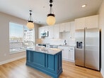 Located at 1140 Chambers Rd in Columbus, Ohio, this efficiently designed one-bedroom, one-bathroom residence makes excellent use of its single-floor layout. The kitchen serves as the centerpiece of the home, showcasing a bold navy-blue island topped with granite countertops, crisp white cabinetry, a classic white tile backsplash, and stainless steel appliances including a French door refrigerator. Globe pendant lights suspended from the ceiling add a stylish, contemporary touch, while large windows flood the space with natural light and views of the surrounding neighborhood. Light hardwood flooring runs throughout the main living areas, contributing to a warm and cohesive aesthetic. The hallway features sleek barn-style sliding doors and conveniently houses a stacked in-unit washer and dryer. The bedroom is finished with plush carpet and an elegant wainscoting-style wall treatment with decorative paneling, creating a refined and cozy retreat. A dedicated closet provides organized storage. The bathroom offers a clean, upscale finish with large-format marble-look porcelain tile flooring, a white vanity with granite countertop, a glass-enclosed shower, and brushed bronze hardware accents. The overall design balances modern style with practical functionality throughout.