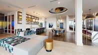 Located at 375 54th Ave N in Saint Petersburg, Florida, this impressive single-floor amenity space offers a diverse range of recreational and social areas designed to engage and entertain. The open-concept social lounge serves as the centerpiece, featuring floor-to-ceiling windows that flood the space with natural light and frame panoramic outdoor views. Plush navy blue seating, a shuffleboard table, and a stylish bar counter with velvet-upholstered stools create an inviting atmosphere for gathering. Large-format pendant lighting and cove-lit ceilings add a polished, modern aesthetic throughout.

A dedicated arcade room stands out with bold Pac-Man themed wallpaper, arcade cabinets, pinball machines, and tabletop gaming units, all set beneath a warm coffered ceiling. Adjacent to this is a golf simulator bay, outfitted with putting green turf, a projection screen, and comfortable lounge seating. A climbing wall enclosed in glass adds an active, sporty dimension to the space, while fitness equipment nearby supports wellness-focused use.

The space also includes a quieter lounge area with access to a furnished outdoor terrace, offering open-air seating with scenic waterfront vistas. Throughout, the design balances contemporary finishes with vibrant, themed accents, creating a dynamic and well-appointed environment.