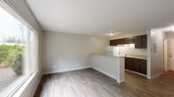 This single-floor unit offers a thoughtfully organized layout that maximizes every square foot. The combined kitchen and living room forms the heart of the space, characterized by light wood-look flooring, neutral gray walls, and a textured ceiling that adds subtle depth. A peninsula counter separates the kitchen from the living area, providing both a functional workspace and a natural room divider. The kitchen is equipped with dark espresso cabinetry, a white refrigerator, and under-cabinet lighting that brightens the countertops. A large window in the living area frames lush greenery outside, allowing ample natural light to fill the room and creating a pleasant connection to the outdoors. The bathroom is clean and well-appointed, featuring a single-sink vanity with dark cabinetry, a mirrored medicine cabinet, and a full-size soaking tub with a shower. Wood-look flooring carries through into the bathroom, maintaining visual consistency throughout the unit. A dedicated closet provides practical storage. The overall design is simple and functional, with a cohesive neutral palette that lends itself well to a variety of furnishing styles.
