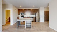 Located at 2435 NE Marshall St in the Northeast Minneapolis neighborhood, this single-floor unit offers a well-designed, functional layout with modern finishes throughout. The kitchen serves as the heart of the space, showcasing rich dark-stained wood cabinetry, granite-style countertops, and a full suite of stainless steel appliances including a refrigerator, electric range, and built-in microwave. A central island with open shelving and a matching countertop provides additional prep space and casual dining options. Light wood-look flooring flows throughout the main living and kitchen areas, creating a warm, cohesive aesthetic. The open layout connects the kitchen seamlessly to the living area, which benefits from natural light. Two bedrooms feature plush carpeting and large windows that overlook an outdoor balcony railing and the surrounding Minneapolis cityscape, offering comfortable, light-filled retreats. The full bathroom is finished with a dark wood vanity, white countertop, a large mirror with overhead lighting, and a tub-shower combination. Exposed ductwork in the bedrooms adds an industrial touch consistent with the Northeast Minneapolis character. In-unit laundry is visible in the floor plan, adding everyday convenience to this thoughtfully appointed home.