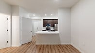 Located at 6400 SW Canyon Ct in Portland, Oregon, this single-floor residence offers a clean, modern design with an efficient and well-appointed layout. The open-concept living and kitchen area is anchored by warm wood-look flooring and crisp white walls, creating a bright and welcoming atmosphere. The kitchen is a standout feature, equipped with dark espresso cabinetry, white quartz countertops, a classic subway tile backsplash, and a full suite of stainless steel appliances including a range, microwave, refrigerator, and dishwasher. A peninsula counter provides additional workspace and a natural divide between the kitchen and living area. The living space benefits from large windows that frame views of the natural rock landscape outside, with a glass door providing direct access to the outdoors and filling the room with natural light. The bedroom is carpeted for comfort and also features a window with the same scenic rock and greenery views. The bathroom is finished with dark wood-toned cabinetry, a white quartz vanity, an oval undermount sink, chrome fixtures, and a large wall mirror. Recessed lighting and wood-look flooring are consistent throughout, tying the space together with a cohesive, contemporary aesthetic.