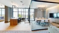 Located at 257 NJ-18 S in East Brunswick, New Jersey, this sophisticated single-floor amenity space offers a thoughtfully designed environment that blends productivity with comfort. Spanning a generous footprint, the layout includes two distinct lounge areas furnished with contemporary seating — one featuring plush leather armchairs beneath a statement circular pendant light, and another with soft blue upholstered chairs arranged around a round coffee table atop a colorful area rug.

Floor-to-ceiling windows line the perimeter, flooding the interior with abundant natural light and providing sweeping views of the surrounding landscape. Light hardwood flooring transitions seamlessly into patterned carpeting throughout the space, adding textural variety and warmth.

Glass-walled conference rooms offer full transparency while maintaining acoustic separation, each equipped with long conference tables, ergonomic seating, and designer pendant lighting. A corridor lined with warm wood paneling and an illuminated decorative wall feature connects the various zones, adding an artistic focal point.

A TULU smart vending kiosk provides on-demand access to everyday essentials, while glass doors open directly to an outdoor terrace. Textured wall treatments, recessed linear lighting, and high-end finishes throughout contribute to the space's polished, modern professional ambiance.