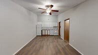 This efficient single-floor unit offers a well-organized layout comprising a living room, kitchen, one bedroom, one bathroom, laundry, a hallway, and two closets. Throughout the unit, durable wood-look plank flooring provides a cohesive and easy-to-maintain aesthetic, complemented by neutral gray walls and textured ceilings.

The open living and kitchen area forms the heart of the unit. The kitchen is outfitted with white cabinetry, a refrigerator, range, dishwasher, and a countertop with an undermount sink — all arranged along a single wall for a clean, space-efficient design. A ceiling fan with a light fixture overhead serves the combined living space, which also features a large window fitted with blinds, allowing natural light to fill the room. A radiator beneath the window provides heating.

The bedroom is a comfortable size, featuring its own ceiling fan, a window with natural light, and a set of warm wood-toned bifold closet doors offering generous storage. A second closet is accessible from the hallway, adding further organizational capacity.

The bathroom includes a full-size soaking tub with a clean white surround. The unit also benefits from a dedicated laundry area, adding everyday convenience. Overall, the space presents a functional and practical layout suited for efficient single-occupant living.