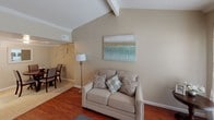 This single-floor residence offers a thoughtfully arranged layout that balances comfort and functionality throughout its main living areas. The living room serves as the heart of the home, showcasing vaulted ceilings with an exposed beam accent and rich hardwood flooring. Natural light streams through a large sliding glass door, brightening the space and creating an inviting atmosphere. Crown molding adds a refined architectural detail throughout the main areas.

Adjacent to the living room, the dining area features tile flooring and accommodates a round dining table with ample seating, making it well-suited for gatherings. The kitchen is equipped with white cabinetry, an electric range, and a built-in pantry closet, offering practical storage and workspace.

The primary bedroom is carpeted and finished with crown molding and a ceiling fan, providing a calm retreat with natural light from a window. It connects directly to a full bathroom, adding a convenient en-suite feel. A second bedroom mirrors the comfortable design with similar finishes and ceiling fan. The bathroom features a tiled tub-and-shower combination with clean, neutral tones.

Throughout the home, warm beige walls and consistent trim work create a cohesive, neutral palette that feels both welcoming and easy to personalize.