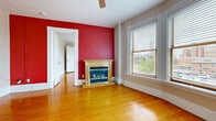 Located at 136 Franklin St in downtown Rochester, NY, this 2-bedroom, 1-bathroom unit showcases classic architectural character throughout its efficiently laid-out single floor. Warm hardwood floors run continuously through the living areas and bedrooms, reflecting natural light and adding timeless appeal.

The living room is a standout space, anchored by a decorative fireplace with an ornate wooden mantle set against a bold red accent wall. Large windows, including a graceful curved bay window configuration, flood the room with natural light and offer views of the surrounding downtown cityscape. A ceiling fan completes the space. Cast-iron radiators throughout the unit provide traditional heating.

Both bedrooms feature hardwood floors and generous windows with views of the neighborhood. The primary bedroom includes a built-in closet with shelving, while the second bedroom also benefits from natural light. Decorative doorway moldings and substantial baseboards reflect the building's historic character.

The kitchen features tile flooring, warm wood cabinetry, white countertops, and stainless steel appliances including a range and over-the-range microwave, accented by a distinctive turquoise wainscoting detail. The bathroom includes tile flooring, open shelving, and a cast-iron radiator.