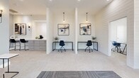 Located at 316 Columbia Dr in Carrollton, GA, this single-floor co-working space offers a clean, modern aesthetic designed to support focused productivity. The space is divided into two distinct office areas, each thoughtfully appointed with sleek, minimalist furnishings and consistent design details throughout.

The primary workspace features striking white shiplap accent walls adorned with framed artwork, pendant lighting, and individual desks paired with ergonomic rolling chairs. Soft, neutral carpeting runs underfoot, contributing to a calm and professional atmosphere. A small refreshment station with cabinetry is conveniently positioned nearby, adding a practical amenity for occupants.

The secondary office area is surrounded by large, multi-pane windows that flood the room with natural light and offer views of the surrounding community. Additional workstations provide flexible seating arrangements suitable for individual or small-group use. Recessed ceiling lighting supplements the natural light, ensuring a well-illuminated environment at all times.

The entry area features a mix of patterned and solid carpet tile, a glass entry door, and ceiling fan, creating a welcoming and functional transition into the workspace. A private office or consultation room with a large window and a long wooden table rounds out the offering, ideal for focused meetings or private work sessions. Together, these spaces deliver a polished, professional environment well-suited for remote work or collaborative use.