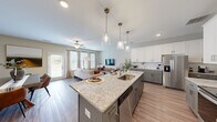Located at 38 Muscat Way in Winder, Georgia, this two-story home offers a well-designed layout spread across two floors. The main level sets an inviting tone with an open-concept kitchen and living area finished with durable wood-look flooring throughout. The kitchen is a standout feature, showcasing two-tone cabinetry—white upper cabinets paired with grey lowers—granite countertops, a large center island with a built-in sink and pendant lighting, and a full suite of stainless steel appliances including a refrigerator, range, microwave, and dishwasher. The adjoining living room is bathed in natural light from multiple large windows and a glass door, complemented by a ceiling fan overhead.

The upper floor houses all three bedrooms, three full bathrooms, and a dedicated laundry room with side-by-side Whirlpool washer and dryer units. The generously sized primary bedroom includes a walk-in closet with wire shelving. Its en-suite bathroom features a glass-enclosed shower, a soaking tub, a double vanity, and wood-look flooring. Secondary bedrooms are carpeted and include ceiling fans. A carpeted flex space on the upper level offers versatility as a home office or sitting area. A staircase with carpet treads connects the two floors.