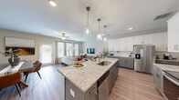 Located at 38 Muscat Way in Winder, Georgia, this two-story home offers a well-designed layout spread across two floors. The main level sets an inviting tone with an open-concept kitchen and living area finished with durable wood-look flooring throughout. The kitchen is a standout feature, showcasing two-tone cabinetry—white upper cabinets paired with grey lowers—granite countertops, a large center island with a built-in sink and pendant lighting, and a full suite of stainless steel appliances including a refrigerator, range, microwave, and dishwasher. The adjoining living room is bathed in natural light from multiple large windows and a glass door, complemented by a ceiling fan overhead.

The upper floor houses all three bedrooms, three full bathrooms, and a dedicated laundry room with side-by-side Whirlpool washer and dryer units. The generously sized primary bedroom includes a walk-in closet with wire shelving. Its en-suite bathroom features a glass-enclosed shower, a soaking tub, a double vanity, and wood-look flooring. Secondary bedrooms are carpeted and include ceiling fans. A carpeted flex space on the upper level offers versatility as a home office or sitting area. A staircase with carpet treads connects the two floors.