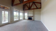 This single-floor residence is defined by its striking architectural character, most notably in the expansive living area where soaring vaulted ceilings showcase bold, exposed wood truss systems with dark metal hardware — creating a dramatic yet warm focal point. Soft carpeting, neutral warm-toned walls, and a classic fireplace with a wood mantel and arched surround add comfort and refinement to the space. Large windows and glass French doors flood the living area with natural light and provide direct access to an outdoor balcony, offering views of the surrounding greenery.

The gourmet kitchen is well-appointed with rich dark wood cabinetry, deep green granite countertops, a large central island with a built-in sink, stainless steel appliances including a gas range, double oven, microwave, and refrigerator, along with a built-in wine rack. Light ceramic tile flooring and recessed and pendant lighting complete the kitchen's polished look.

The bedrooms are carpeted and bright, with crown molding details and ceiling fans providing an inviting atmosphere. The primary bathroom features a spacious walk-in glass-enclosed shower with tile surround, a long double-sink vanity with dark cabinetry, and tile flooring. A secondary bathroom offers a single vanity and clean, functional finishes throughout.