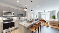 This thoughtfully designed 2-bedroom, 2-bathroom residence offers a cohesive single-floor layout that maximizes both functionality and style. The open-concept kitchen and living area serves as the heart of the home, anchored by a granite-topped kitchen island with bar seating and stylish pendant lighting overhead. The kitchen features gray cabinetry, a tile backsplash, stainless steel appliances including a French door refrigerator, and light wood-tone lower cabinetry. Wood-look flooring extends throughout, providing a warm, continuous flow into the living area, which is bathed in natural light from large windows. The primary bedroom is a generous, serene retreat with ample space and its own dedicated closet fitted with wire shelving systems. The second bedroom offers a similarly comfortable layout. Both bathrooms are finished with granite vanities and gray cabinetry; one features a full soaking tub with subway tile surround and dark hardwood-style flooring. Additional closets provide excellent storage throughout. A dedicated in-unit laundry area houses a full-size washer and dryer with overhead shelving. The overall aesthetic is modern and neutral, with clean lines and a bright, airy atmosphere throughout.