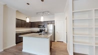 This single-story, two-bedroom, two-bathroom residence offers a thoughtfully designed layout that balances open living with functional comfort. The kitchen serves as the centerpiece of the home, showcasing dark espresso cabinetry that extends to the ceiling, providing generous storage throughout. Granite countertops run along the perimeter and continue onto a central island equipped with a sink, making it ideal for both meal preparation and casual dining. Stainless steel appliances, including a refrigerator, range, and microwave, complement the contemporary aesthetic. Pendant lights and a track lighting system illuminate the space effectively. Wood-look flooring flows through the main living areas, creating a warm, cohesive feel. Built-in shelving near the kitchen adds practical display and storage options. The bedrooms feature plush carpeting and include closets with wire shelving systems for organized storage. Both bathrooms maintain consistency with the home's design language, featuring dark cabinetry, granite-topped vanities, and tub-shower combinations with clean white surrounds and wood-look flooring. The overall aesthetic is modern and cohesive, with neutral tones providing a versatile backdrop throughout.