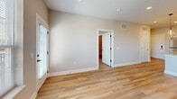 Located at 215 E Lincolnway in Valparaiso, Indiana, this well-appointed one-bedroom, one-bathroom unit offers a thoughtfully designed open-concept layout finished with light wood-tone luxury vinyl plank flooring throughout. The kitchen serves as the heart of the space, showcasing white shaker cabinetry with matte black hardware, granite countertops, a classic subway tile backsplash, stainless steel appliances including a dishwasher and refrigerator, and a central island topped with pendant lighting — ideal for both cooking and casual dining. The kitchen flows seamlessly into a combined dining and living area, which benefits from natural light through large windows overlooking the surrounding neighborhood. A dedicated pantry provides additional storage convenience. The spacious bedroom features generous windows that fill the room with natural light and connects to a dedicated laundry room outfitted with a stacked washer and dryer. The full bathroom is finished with granite counters, white subway tile in the walk-in shower with a black-framed glass door, and coordinating matte black fixtures. A private balcony extends the living space outdoors, while a utility room rounds out the functional layout of this modern Valparaiso residence.