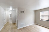 Located at 1625 Morris Road SE in Washington, DC, this two-bedroom, one-bathroom unit offers a practical and well-organized single-floor layout. Light wood-tone flooring runs throughout the entire unit, lending a clean, cohesive look to every room. Neutral warm-gray walls complement the bright, airy feel of the space.

The combined living and dining area serves as the central hub of the unit, with visible HVAC vents for heating and cooling and direct sightlines through to the hallway and kitchen. The kitchen is efficiently designed with sufficient cabinetry, providing ample storage for everyday needs. A dedicated utility room and hallway further enhance the functional flow of the layout.

The primary bedroom is a well-proportioned room featuring two windows that invite natural light and views of the surrounding greenery. The second bedroom also benefits from natural light through its own window and includes access to a closet. A third bedroom features dual entry doors and its own closet, offering added flexibility. In total, the unit includes three closets, providing generous storage throughout.

The bathroom features a full tub-shower combination with white tile surround, a gray vanity with an integrated sink, a mirrored medicine cabinet, and a decorative stained-glass window that adds a distinctive touch. Clean white finishes keep the space feeling bright and tidy.