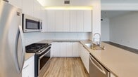 Located at 138 N Beaudry Avenue in downtown Los Angeles, this single-floor unit offers a thoughtfully designed layout with a clean, modern aesthetic throughout. Wood-style plank flooring runs continuously through the living spaces and hallways, providing a warm, cohesive foundation that complements the crisp white walls and recessed lighting overhead.

The kitchen is a standout feature, outfitted with sleek flat-front white cabinetry that extends to the ceiling with ambient uplighting above. Stainless steel appliances — including a gas range, built-in microwave, refrigerator, and dishwasher — pair with neutral quartz-style countertops and a classic white subway tile backsplash. A peninsula with an undermount sink and a flexible faucet adds functional prep space and a natural transition to the adjacent living area.

The living area is bright and open, with clean walls and ample space for varied furniture arrangements. A hallway connects the main living areas to additional rooms and storage, featuring louvered closet doors that add a touch of texture and practicality. The bathroom is finished in a minimalist style, featuring an undermount sink with modern cabinetry, a large backlit mirror, wood-look flooring, and an accessibility grab bar. The overall ambiance of the space is light, airy, and move-in ready, reflecting contemporary urban living.
