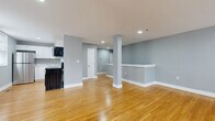 Located at 223 Meadow St in Naugatuck, CT, this two-story, 2-bedroom, 2-bathroom residence offers a thoughtfully organized layout spread across two floors. The main level greets you with an open-concept living area finished in warm hardwood flooring and soft gray walls, creating a clean, modern ambiance. Recessed lighting illuminates the space throughout, while a structural column and a half-wall partition subtly define zones within the open floor plan. The kitchen is equipped with white cabinetry, a stainless steel refrigerator, a black range, and a microwave, with a window providing natural light. A dedicated entrance and laundry area add practical convenience on this level. The upper floor hosts the two bedrooms, including a generously sized primary bedroom with hardwood floors and dual windows offering neighborhood views. The second bedroom features light luxury vinyl plank flooring and small windows that bring in natural light. Both bathrooms are cleanly appointed, with one featuring a white vanity, mirrored medicine cabinet, and chrome fixtures. Four closets distributed throughout the home ensure ample storage. Staircases connect the levels with a handrail for safety, and a hallway links the upper-floor rooms cohesively.