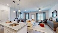 The Blakey offers a thoughtfully designed single-floor residence that seamlessly blends modern aesthetics with everyday functionality. The open-concept layout connects the kitchen, dining, and living areas, creating a cohesive and inviting atmosphere throughout the common spaces.

The kitchen serves as a central hub, anchored by a granite-topped island with a undermount sink and matte black faucet, illuminated by industrial-style pendant lights. White shaker cabinetry with matte black hardware, a white subway tile backsplash, and stainless steel appliances complete the space with a clean, contemporary look. Light wood-style flooring flows seamlessly from the kitchen into the adjoining areas.

The dining area accommodates a round dark wood table and is highlighted by a large-scale abstract artwork. The living room is bright and welcoming, featuring a ceiling fan, large windows with teal drapery, and direct access to an exterior door, allowing ample natural light.

The bedrooms are comfortably scaled, each featuring ceiling fans, natural light from well-positioned windows, and light wood flooring. The bathroom is clean and functional, featuring a tiled tub-shower combination, granite vanity top, and wood-look flooring, maintaining the cohesive design language found throughout the residence.