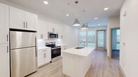 Located at 17501 Dallas Parkway in Dallas, TX, this thoughtfully designed one-bedroom, one-bathroom residence offers a clean, contemporary aesthetic throughout its efficiently planned single floor. The open-concept kitchen is a standout feature, showcasing white shaker cabinetry with matte black hardware, a white quartz countertop island with an undermount sink, stainless steel appliances including a range, microwave, and refrigerator, and a classic subway tile backsplash. Stylish industrial-inspired pendant lights hang above the island, complementing the recessed lighting overhead. Light wood-tone luxury vinyl plank flooring runs throughout the main living areas, adding warmth and continuity. The living area benefits from abundant natural light through large windows and a glass door, with a ceiling fan adding comfort. The bedroom is carpeted for coziness and features a ceiling fan, generous windows that flood the room with daylight, and direct access to a dedicated walk-in closet outfitted with multiple shelving rods and shelves. The bathroom is finished with white cabinetry, quartz countertops, an LED-backlit vanity mirror, and matching wood-tone flooring, creating a cohesive and polished look throughout the entire residence.