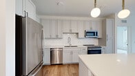 This thoughtfully designed 1-bedroom, 1-bathroom residence offers an efficient and functional single-floor layout with refined finishes throughout. The open-concept living, dining, and kitchen area serves as the heart of the home, creating a seamless flow ideal for both everyday living and entertaining. The kitchen is a standout feature, showcasing soft gray shaker-style cabinetry extending to the ceiling, a herringbone tile backsplash, quartz countertops, and a full suite of stainless steel appliances including a range, microwave, dishwasher, and refrigerator. A central kitchen island with seating provides additional prep and dining space, while globe pendant lights add a modern, stylish touch. Light hardwood-style flooring runs throughout the main living areas, complementing the bright, neutral color palette. The living room benefits from a window with exterior views, creating an inviting and airy atmosphere. The bedroom is a comfortable, carpeted retreat with soft neutral walls and ample space. The full bathroom features wood-look flooring, a white vanity with storage, and a tub-shower combination. A dedicated closet and in-unit washer and dryer add everyday convenience to this well-considered home.