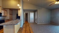 Located at 1825 East Republic Road in Springfield, Missouri, this single-floor unit offers a well-designed open-concept layout that seamlessly connects the main living areas. The living and dining spaces feature warm hardwood flooring, with the living area transitioning to plush carpet for added comfort. Soaring ceilings in the main living space create an airy, open ambiance, enhanced by stylish pendant lighting that illuminates the kitchen and dining area.

The kitchen is equipped with light maple cabinetry, granite-style countertops, and black appliances including a refrigerator, range, and over-the-range microwave. A breakfast bar peninsula provides additional counter space and casual seating. A dedicated dining nook adjacent to the kitchen is highlighted by a pendant light fixture.

The bedroom features plush carpeting, a tray ceiling with a ceiling fan, and a window with blinds that allows natural light to filter in. A built-in desk ledge with a granite-style surface adds functional workspace. The bedroom also provides access to a generously sized walk-in closet outfitted with wire shelving and hanging rods for ample storage.

The bathroom includes hardwood flooring, a granite-style vanity with wooden cabinetry, and a full tub-shower combination. The unit's neutral gray palette throughout creates a cohesive, modern aesthetic.