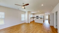 Located at 2009 S Veterans Blvd in Gonzales, Louisiana, this single-story, 3-bedroom, 2-bathroom home offers a clean, modern design with a bright and cohesive aesthetic throughout. Warm hardwood-style flooring runs continuously across the living areas, hallways, and bedrooms, creating a unified and inviting atmosphere.

The open-concept living area flows seamlessly into a well-appointed kitchen featuring white cabinetry, a center island with pendant lighting, stainless steel appliances, and recessed lighting — ideal for both everyday living and entertaining. A ceiling fan with a light fixture anchors the living space.

The hallway connecting the bedrooms is wide and well-lit, with overhead ventilation and clean white walls. Each of the three bedrooms is outfitted with a ceiling fan and window with blinds, allowing for natural light and comfortable airflow. The spacious primary bedroom features dual windows and connects to a private bathroom with white cabinetry, a white countertop vanity, matte black fixtures, and direct access to a walk-in closet with built-in shelving.

The dedicated laundry room includes a washer and dryer with overhead shelving and an adjacent storage closet with built-in shelves. The attached garage offers ample space and an automatic door opener. This home presents a practical and polished living environment.