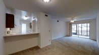 This single-story unit offers a practical and comfortable layout designed to maximize its living space. The open-concept living area is finished with wall-to-wall carpeting and features a ceiling fan with light fixture, contributing to both comfort and functionality. A sliding glass door at the far end of the living room fills the space with natural light and provides direct access to an outdoor area, enhancing the sense of openness.

The kitchen connects to the main living area via a pass-through counter, creating an efficient and interactive flow between spaces. Kitchen cabinetry is visible through the opening, and the area benefits from its own overhead lighting. HVAC vents are positioned throughout the unit, ensuring consistent climate control.

White walls and a textured ceiling are consistent throughout, giving the unit a clean, neutral aesthetic that is easy to personalize. The layout is straightforward and efficient, with the bedroom and bathroom tucked away from the main living area. Overall, the unit presents a bright, functional living environment suitable for a single occupant or couple.
