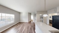 This efficient single-story residence offers a thoughtfully designed open-concept layout that seamlessly connects the living, dining, and kitchen areas. Rich wood-look vinyl flooring flows throughout the main living spaces, complemented by neutral gray walls and crisp white trim that create a clean, modern aesthetic.

The kitchen serves as a functional centerpiece, featuring gray cabinetry, light stone-look countertops, a stainless steel double sink, and black appliances including a refrigerator, electric range, and over-the-range microwave. A peninsula with pendant lighting provides a natural division between the kitchen and the open dining and living areas, which benefit from natural light streaming through the windows.

The bedroom offers a comfortable and private retreat, finished with plush carpeting, a ceiling fan with light fixture, a closet, and a window with blinds providing outdoor views. Three total closets throughout the unit ensure ample storage.

The bathroom is well-equipped with dark gray cabinetry, a stone-look countertop vanity, a large mirror, wood-look flooring, and an additional closet. In-unit laundry adds a layer of everyday convenience. The entrance provides a welcoming transition into the home, rounding out a practical and cohesive living space.