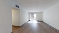This single-floor residential unit offers a well-organized and functional layout designed for comfortable everyday living. The spacious living area is finished with warm hardwood-style flooring that extends throughout the main living and entry spaces, creating a cohesive and inviting atmosphere. A sliding glass door at the far end of the living room floods the space with natural light and provides direct access to a private balcony, offering outdoor views and fresh air. The entry foyer is bright and open, featuring a gray paneled front door and overhead lighting.

The kitchen is outfitted with medium-toned wood cabinetry, dark granite-style countertops, a subway tile backsplash in a neutral gray palette, and stainless steel appliances including a refrigerator and electric range, combining both style and practicality.

The bedroom is carpeted with a bold, patterned floor covering and is served by two doors — one leading to a tiled en-suite bathroom with white subway tile walls, and another opening into a dedicated walk-in closet with built-in shelving. The bathroom features dark diagonal-set floor tile and clean, classic fixtures. An additional window in the bedroom allows natural light to brighten the space. Central HVAC vents are present throughout, ensuring year-round climate comfort.
