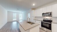 Located at 72 Milton Ave SE in Atlanta's 30315 neighborhood, this contemporary single-floor residence showcases a clean, modern aesthetic throughout. The open-concept layout centers around a sleek kitchen featuring a large island with an undermount sink and quartz-style countertops, floor-to-ceiling white cabinetry, and a full suite of stainless steel appliances including a range, over-the-range microwave, and refrigerator. The kitchen flows seamlessly into a generous living area finished with wood-style flooring and bathed in natural light from multiple large windows. The bedrooms offer plush carpeting and ample natural light, with one room featuring dual windows and a ceiling fan for added comfort. The bathrooms are thoughtfully designed with extended dual-sink vanities, gray countertops, large mirrors, and wood-style flooring. One bathroom includes a soaking tub with shower combination, while the other offers a glass-enclosed walk-in shower. Throughout the residence, the crisp white walls, recessed lighting, and consistent use of modern finishes create a cohesive, move-in-ready environment that is both functional and stylish.